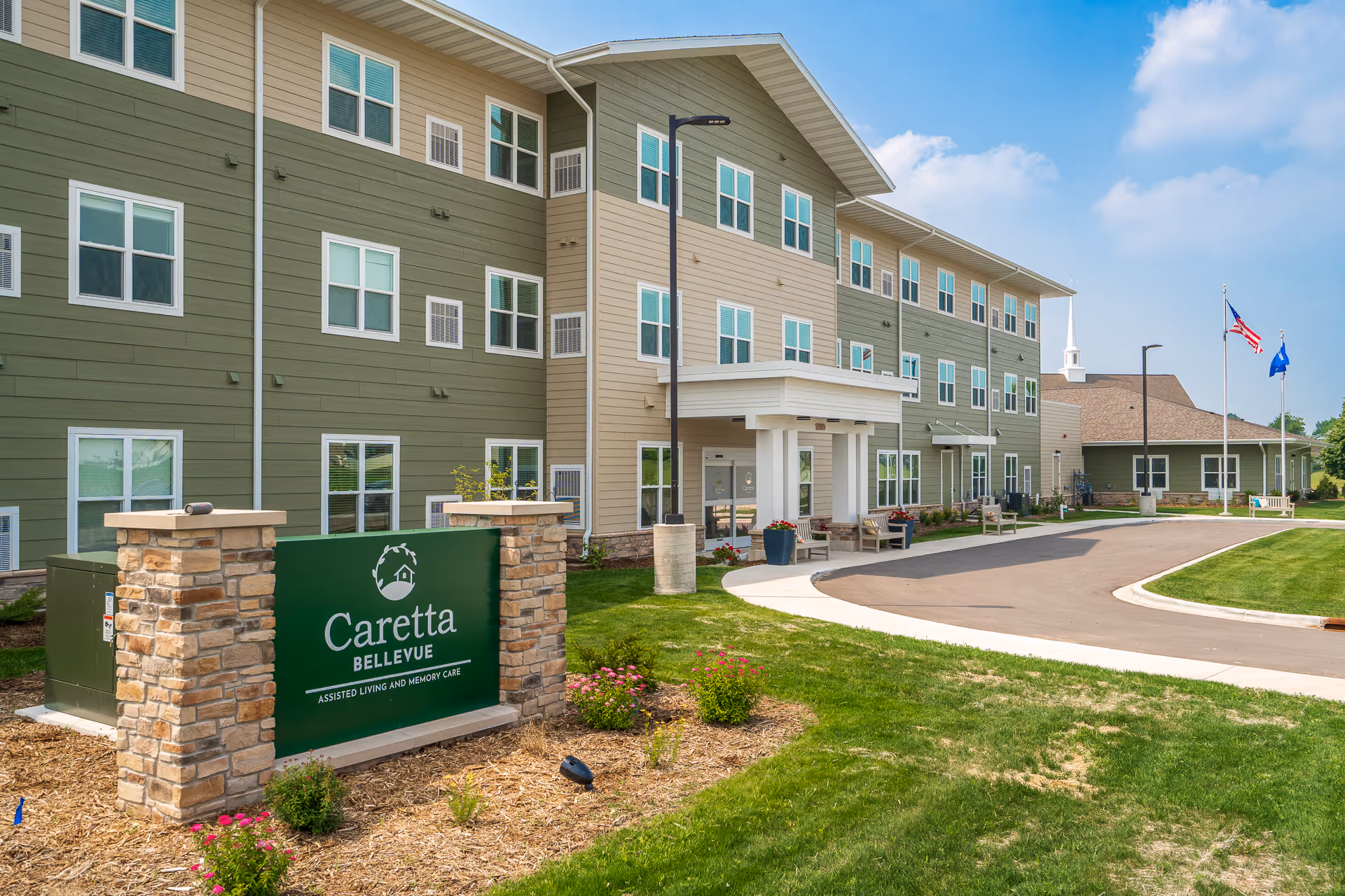 Exterior view of Caretta Bellevue senior living building with curved driveway and green sign.