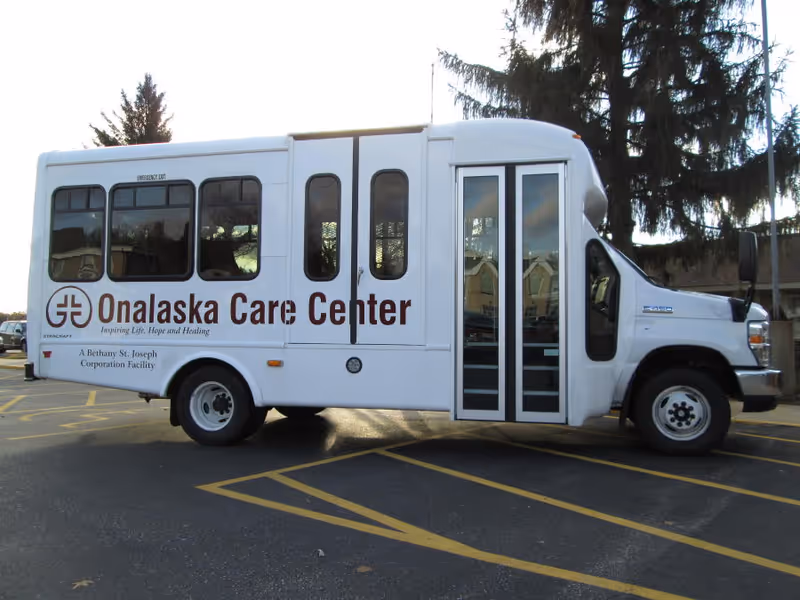 White bus labeled Onalaska Care Center parked in a parking lot.