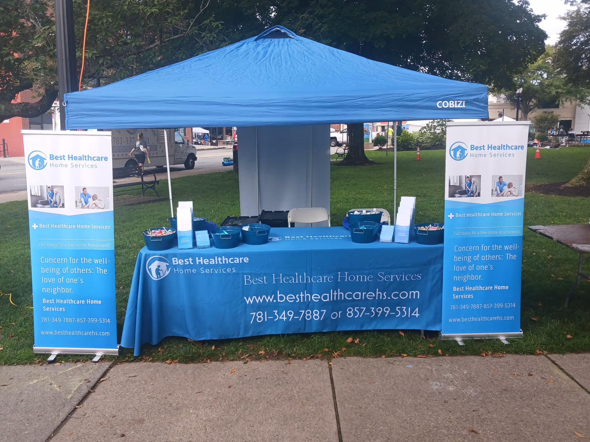 Blue canopy tent with banners and a table promoting Best Healthcare Home Services at outdoor event