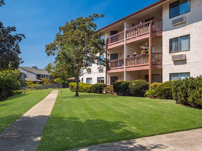Senior living building with balconies, green lawn, and a sidewalk path.