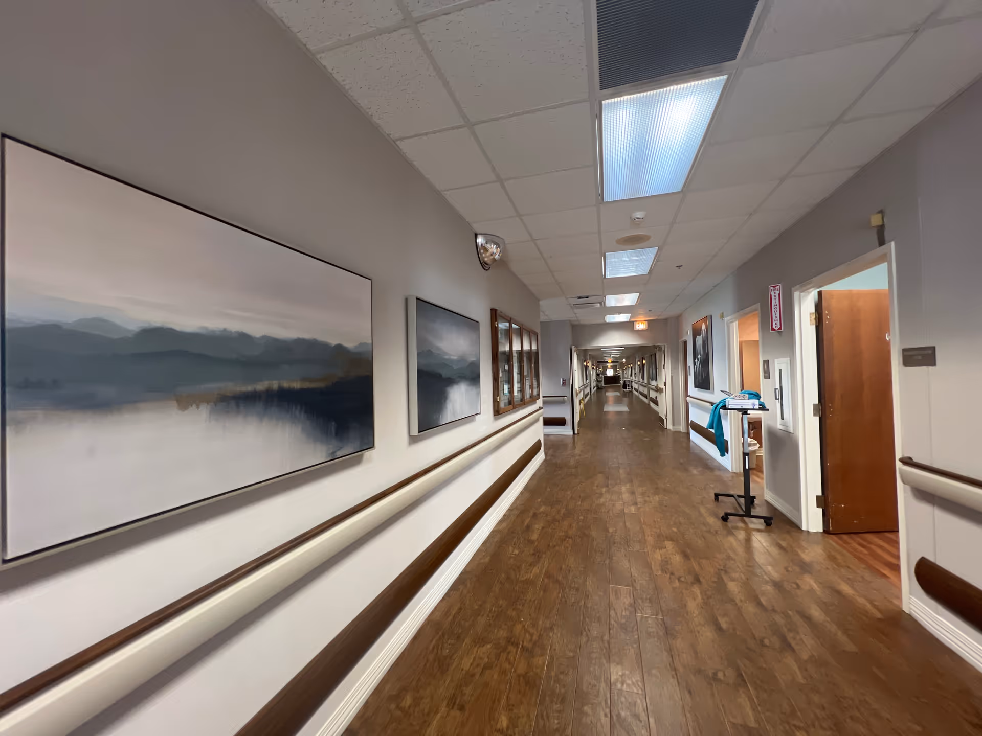 A long, well-lit interior hallway in Nhc Healthcare Ft Oglethorpe with wall art and wood flooring.