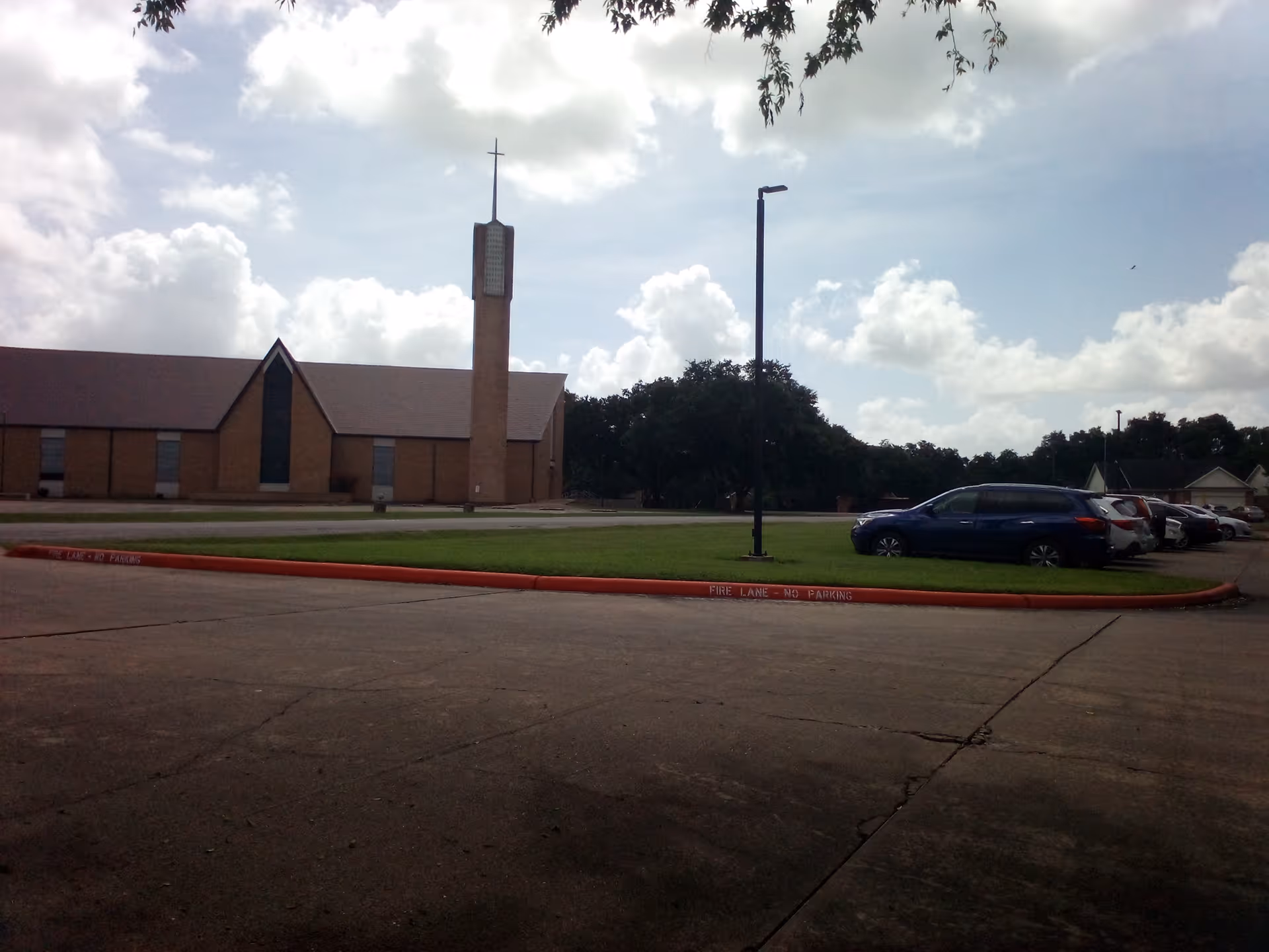 Exterior view of Oliver Street Respite facility with brick walls, parking lot, and a cross-towered steeple.