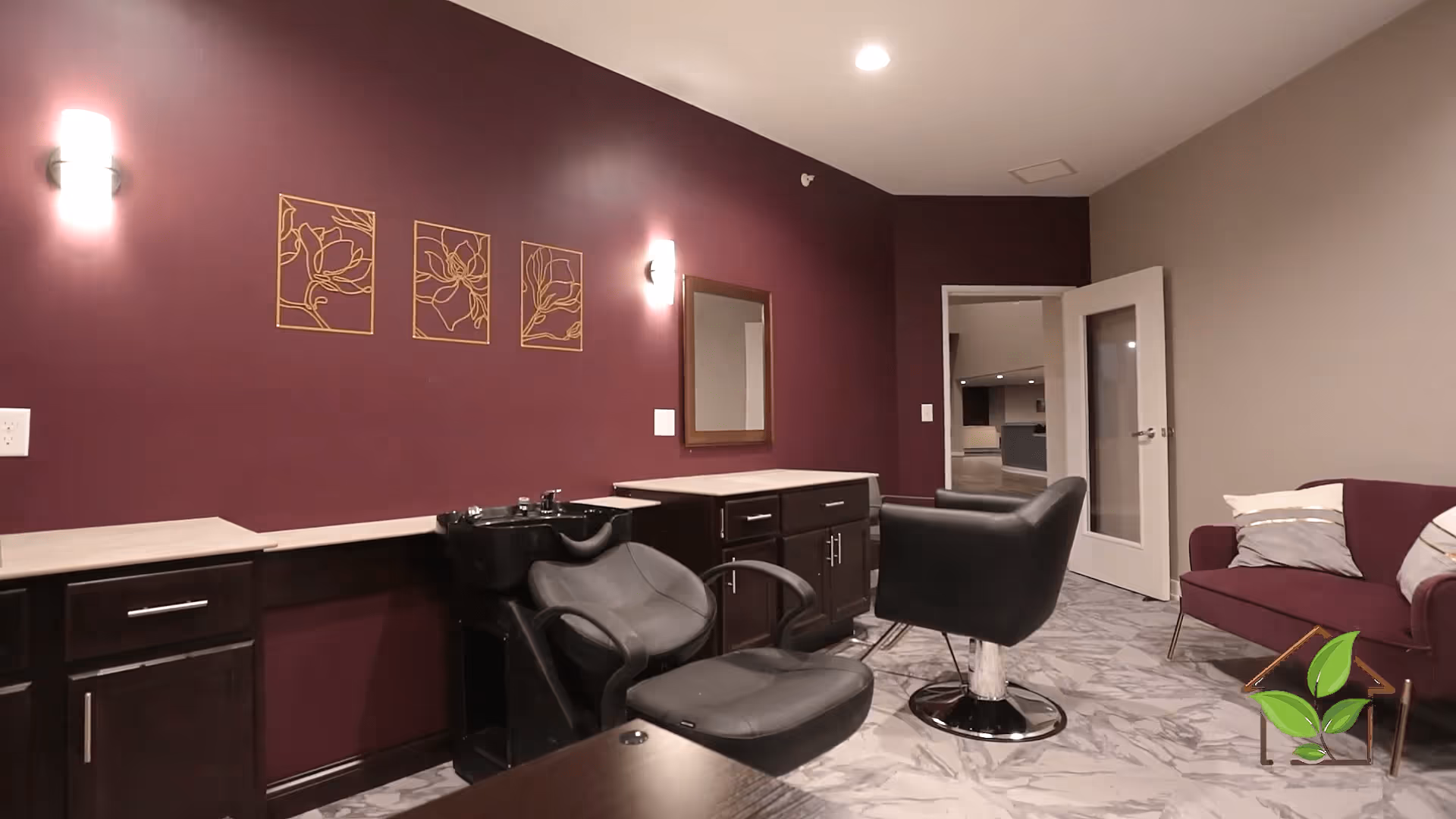 Interior room featuring salon chairs and a hair-washing basin against a maroon wall with a nearby couch.