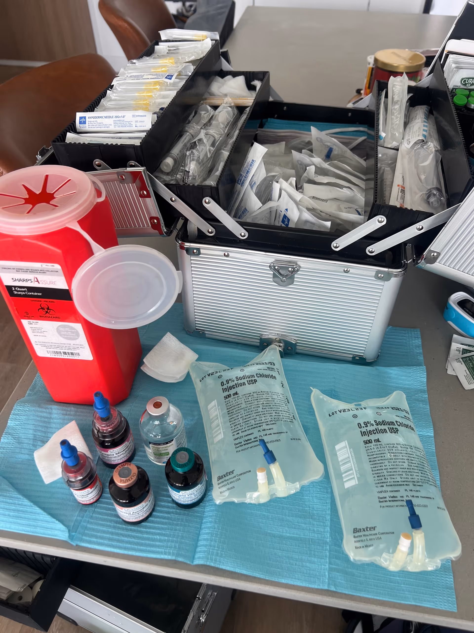 Open medical kit on table with IV bags, medication vials, and sharps container.