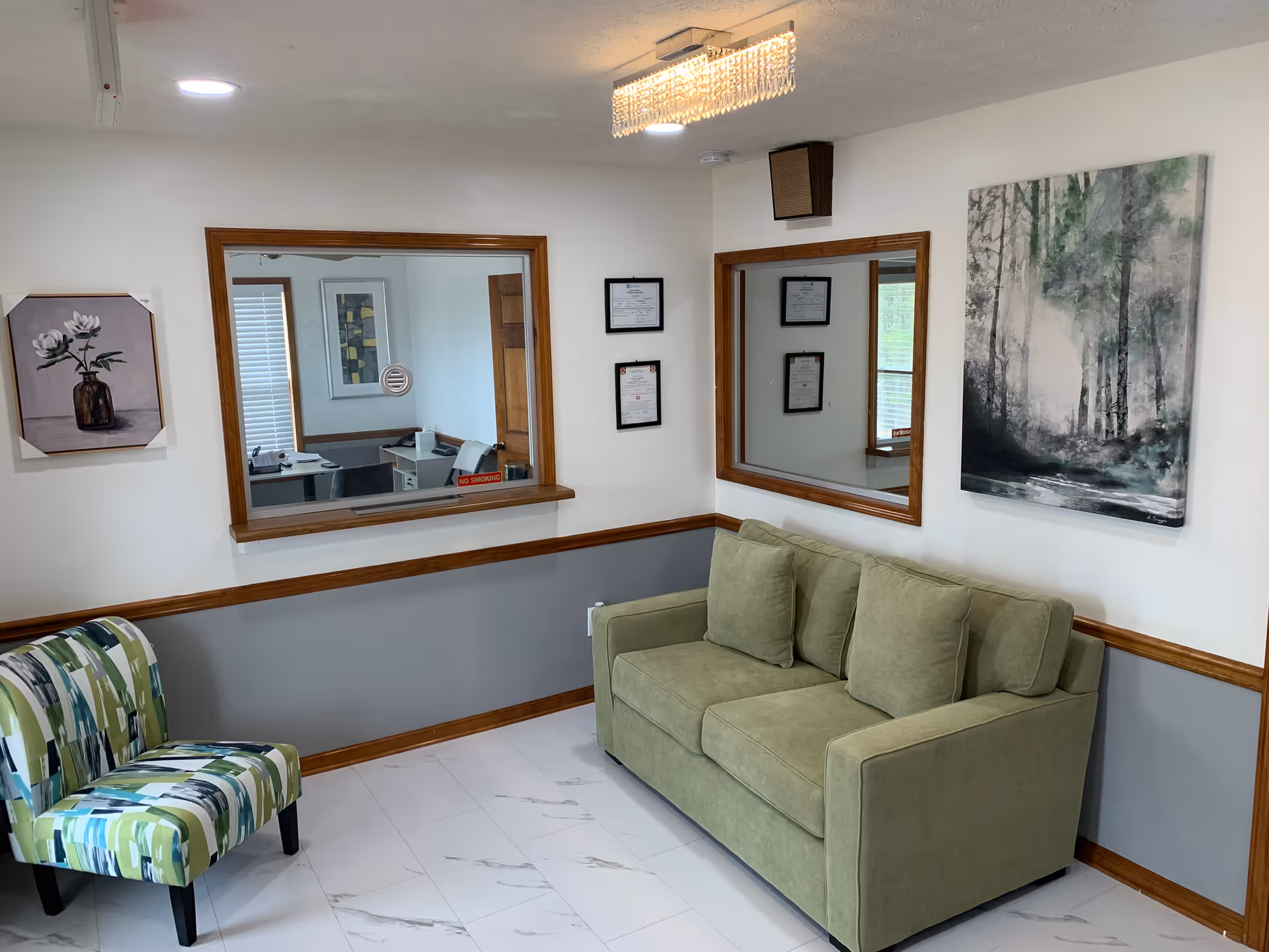 Lobby seating area with green sofa, patterned chair, wall art, and framed certificates.