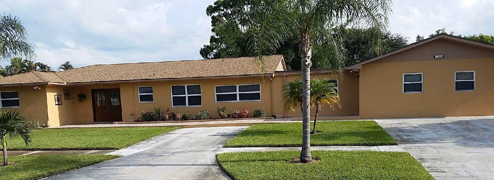 Single-story beige facility exterior with palm trees, a driveway, and a well-kept lawn.