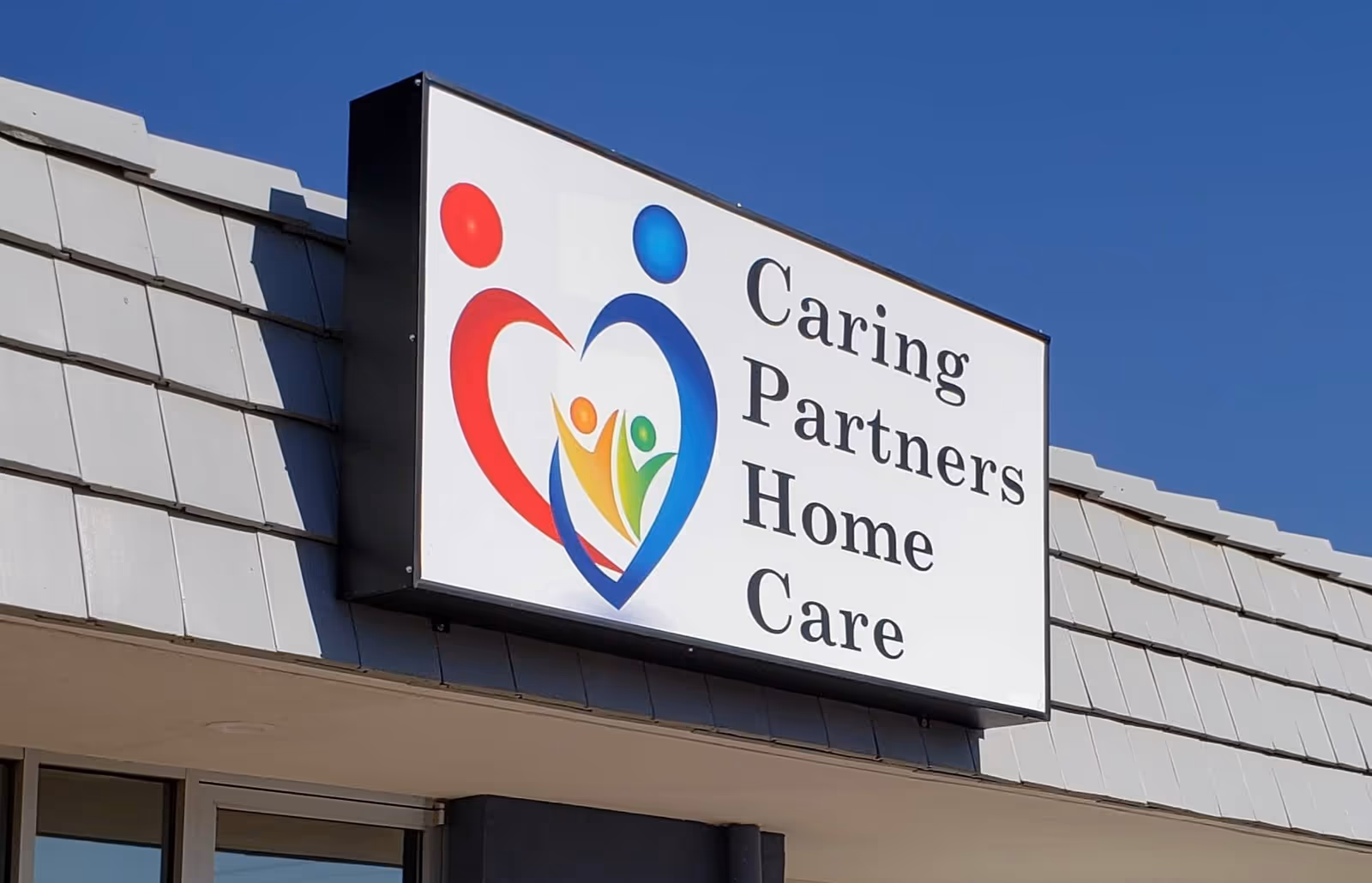 Exterior building sign reading Caring Partners Home Care with heart-shaped logo on a blue sky
