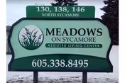 Green exterior sign for Meadows on Sycamore Assisted Living Center with phone number.
