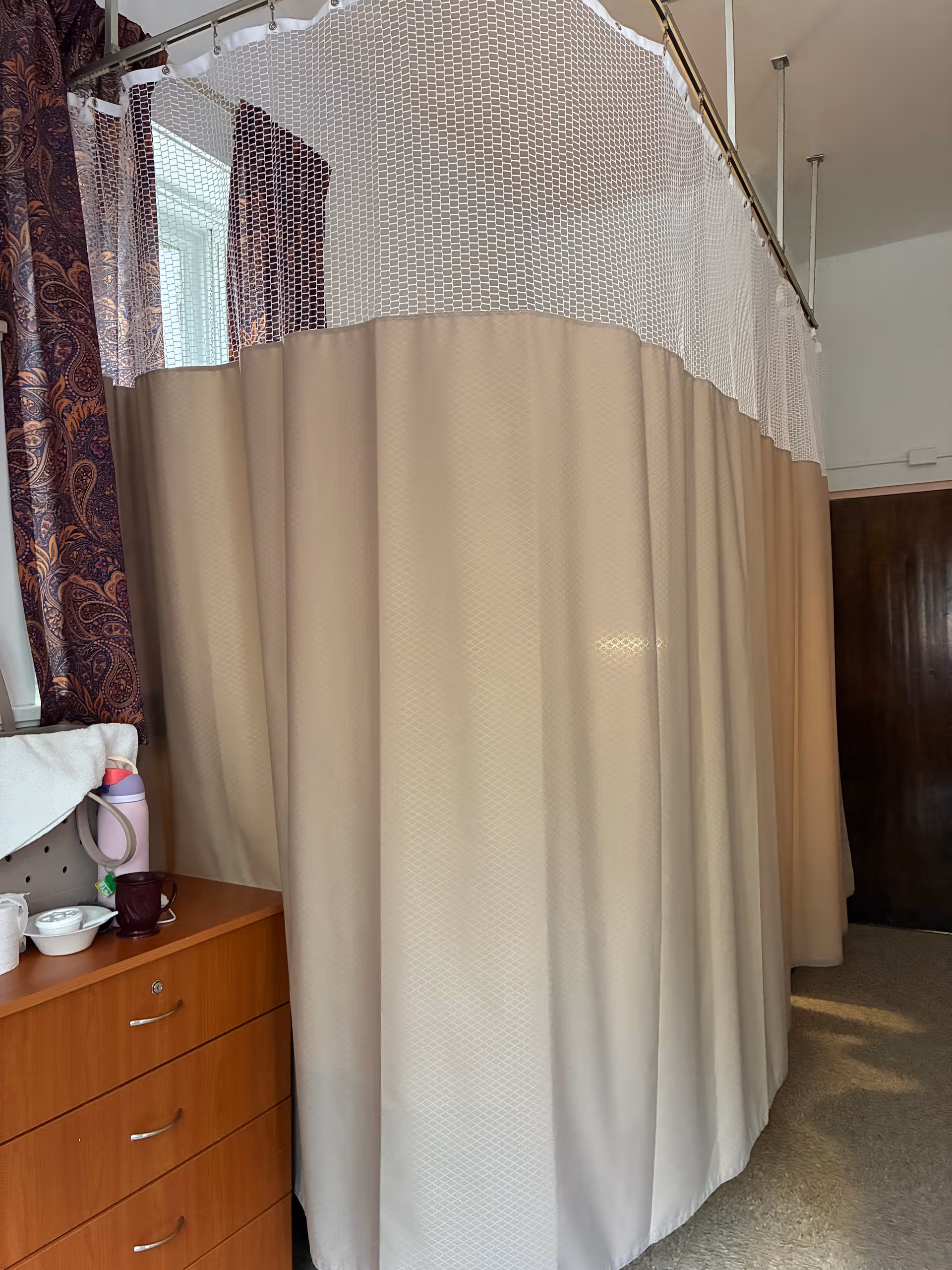 Beige curtain surrounds a shower stall in a bathroom beside a wooden dresser.