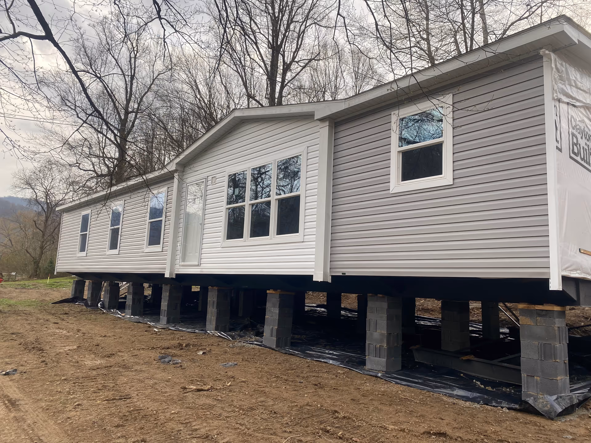 A modular building under construction on pier foundations with white-gray siding and windows.