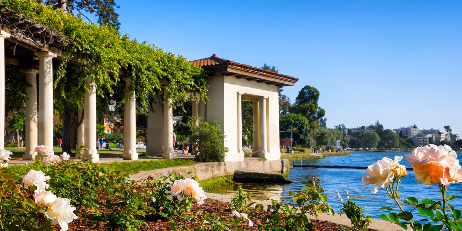 Lakeside park with a colonnade, roses, and a pavilion beside the water.