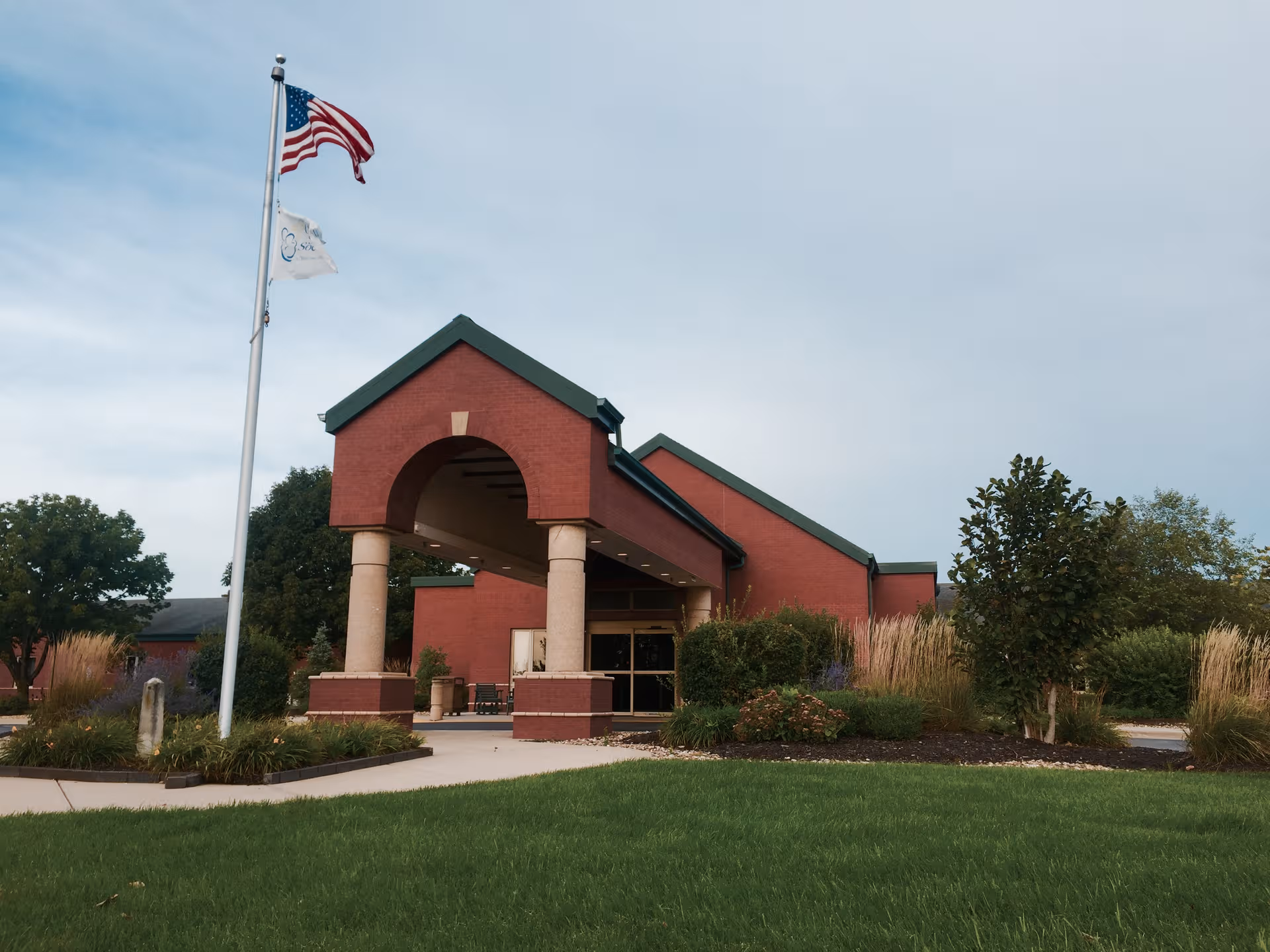 Good Samaritan Society - Olathe exterior: red-brick entrance with archway, flagpole, and landscaped lawn.