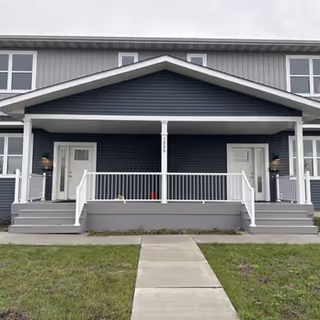 Exterior view of a gray assisted living facility with a covered front porch and white railings.