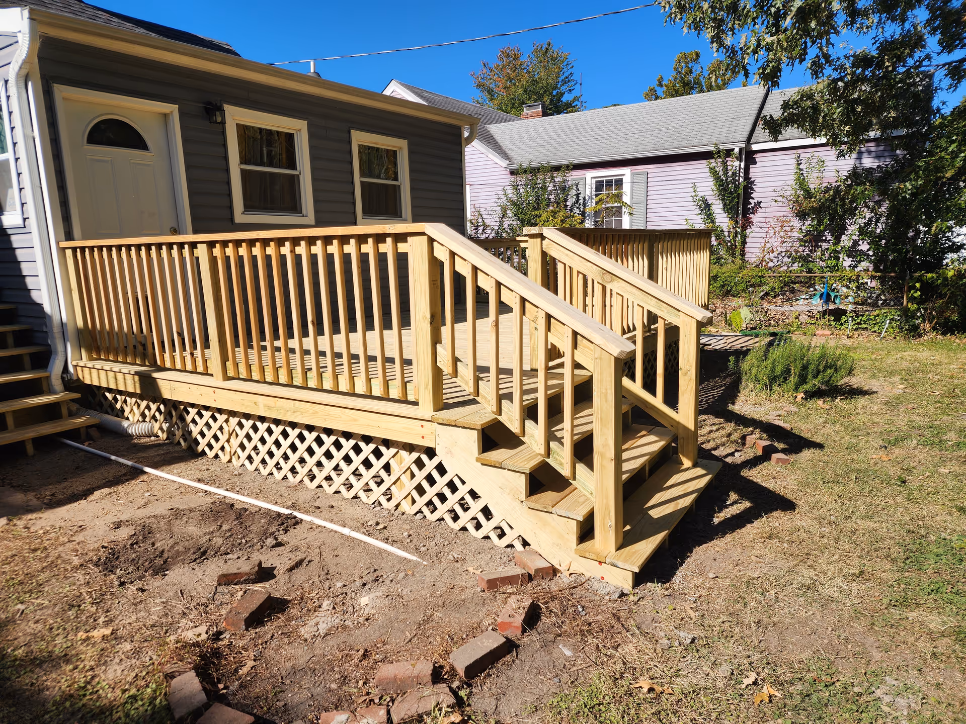 Wooden raised deck with railing attached to a small house and grassy yard.