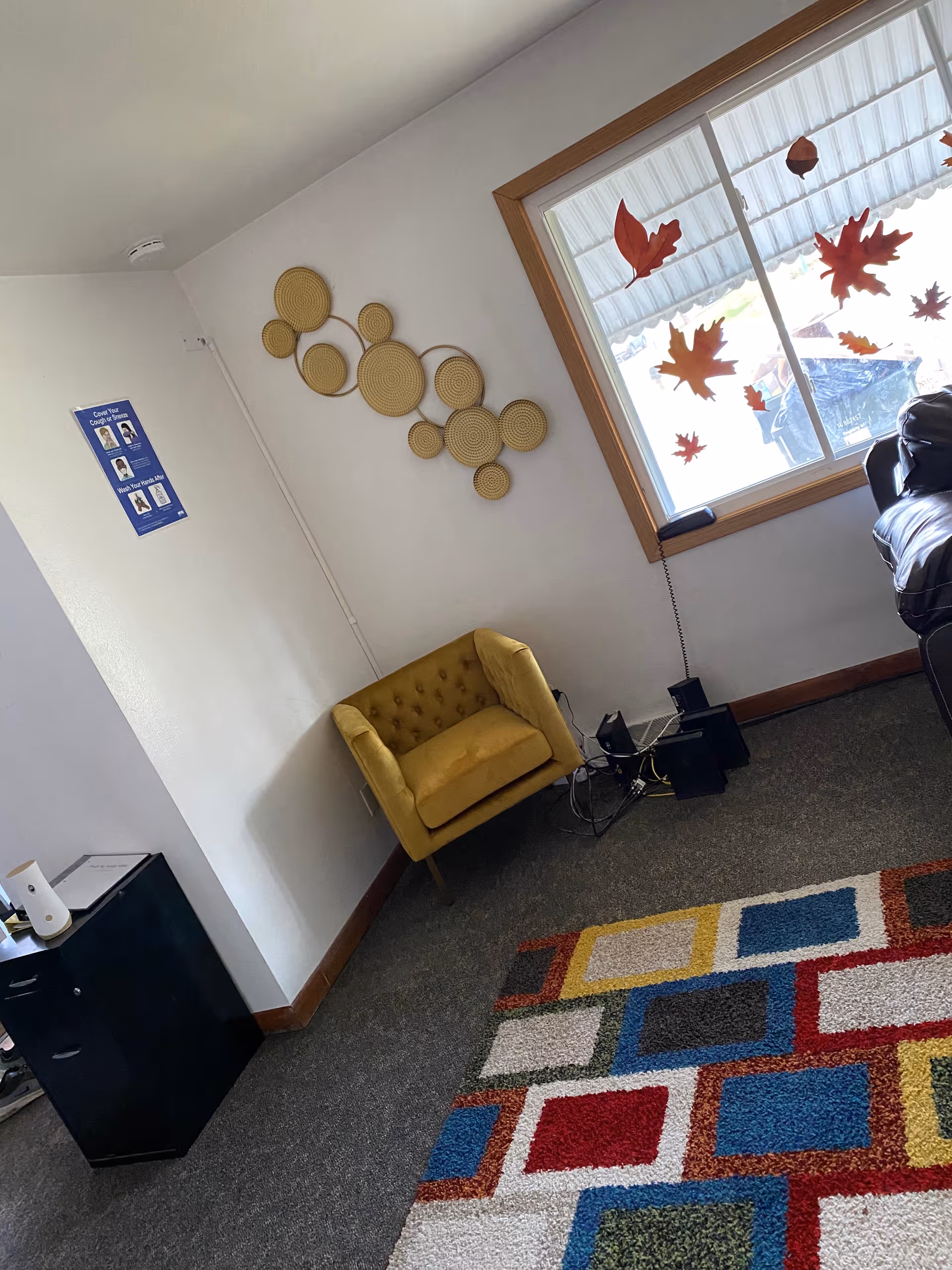 Cozy interior corner featuring a yellow tufted chair, colorful rug, wall art, and decals on window.