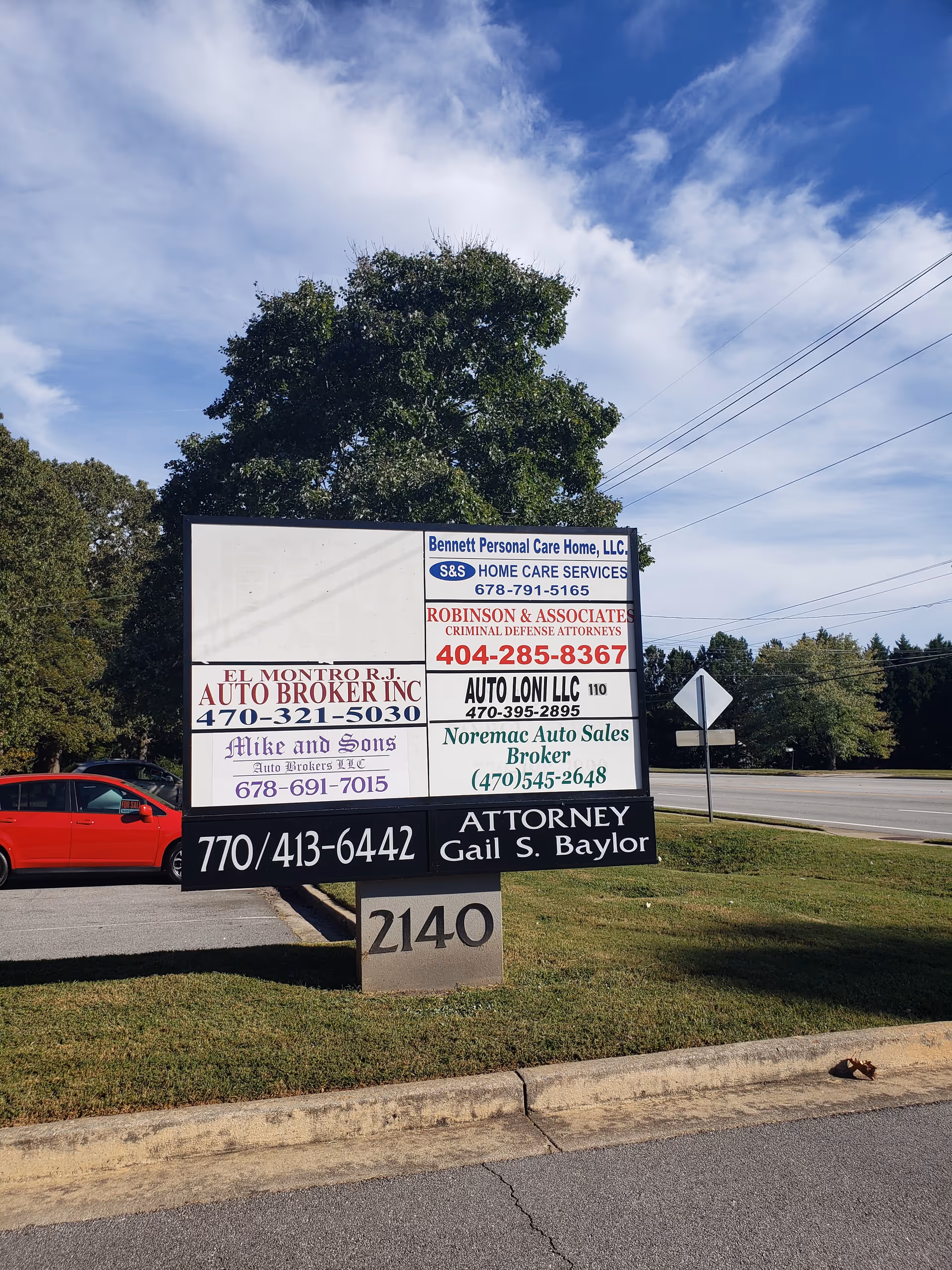 Roadside signboard displaying multiple business advertisements beside a grassy area.