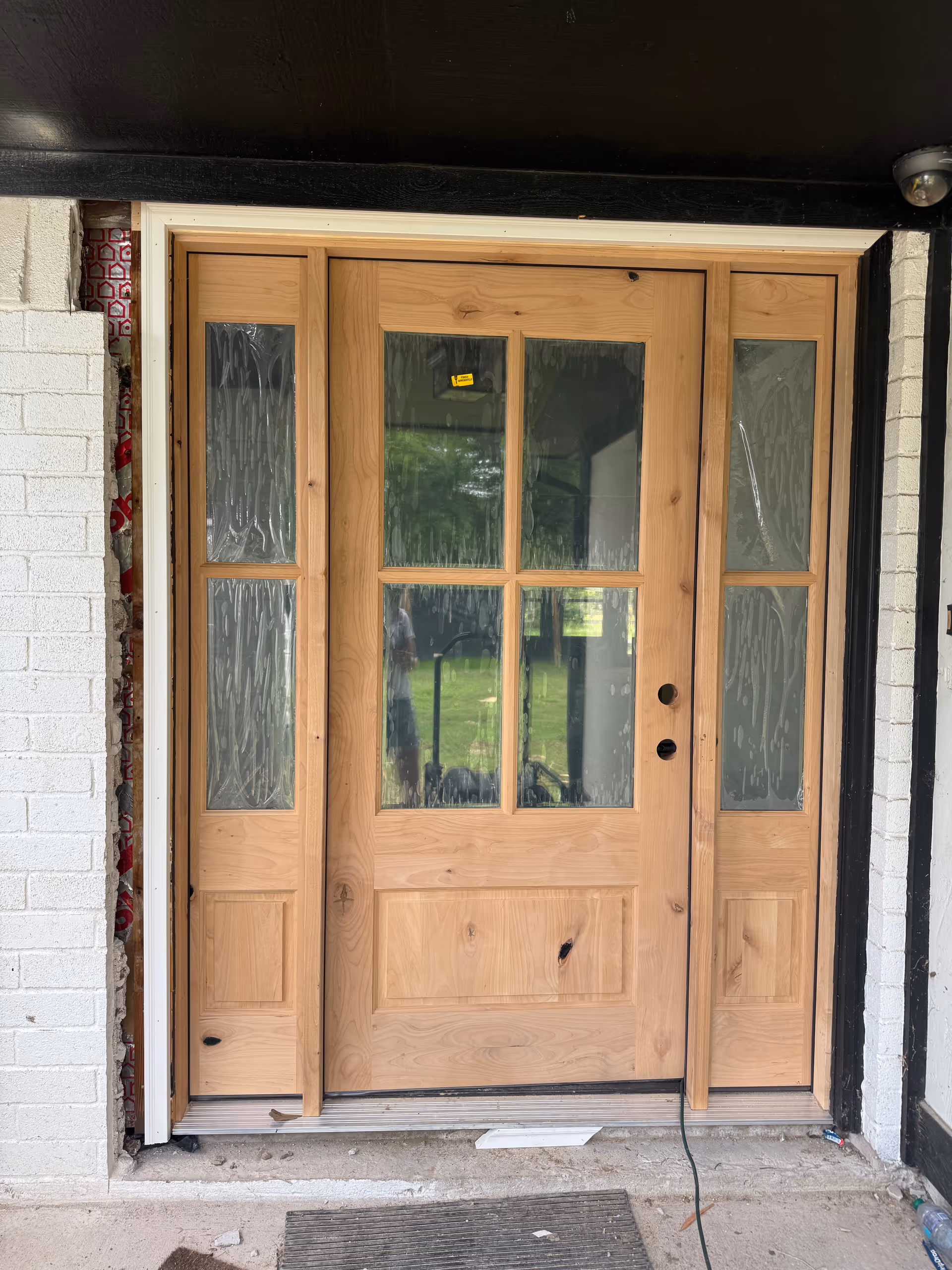 Wooden double front door with glass panes, framed by brick exterior.