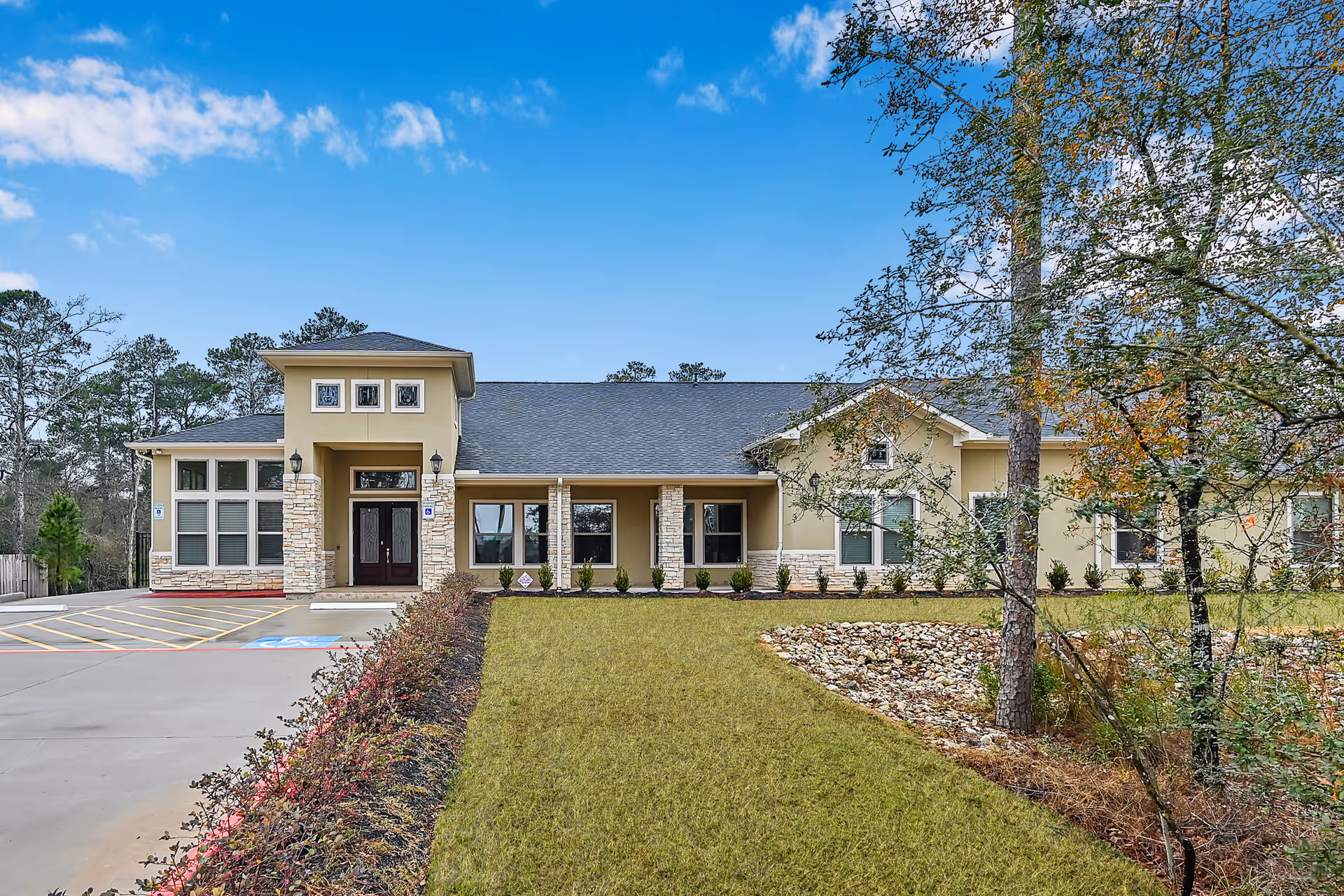 Front exterior of a single-story memory care building with a central entrance, windows, landscaped lawn and parking area.