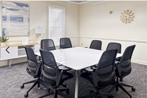 Interior meeting room with a white square table and black office chairs.