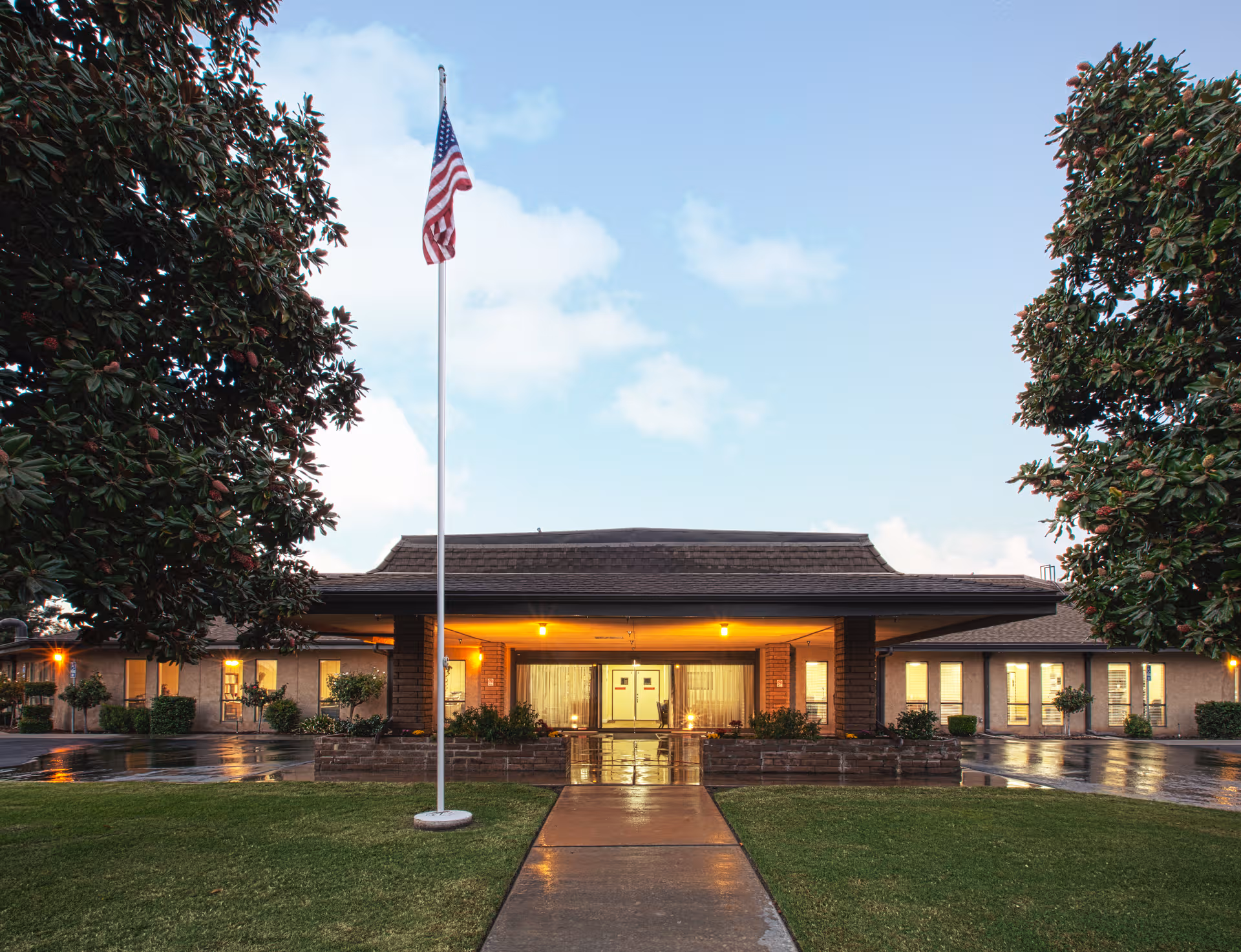 Linwood Meadows Care Center front entrance with flagpole, trees, and warm exterior lighting