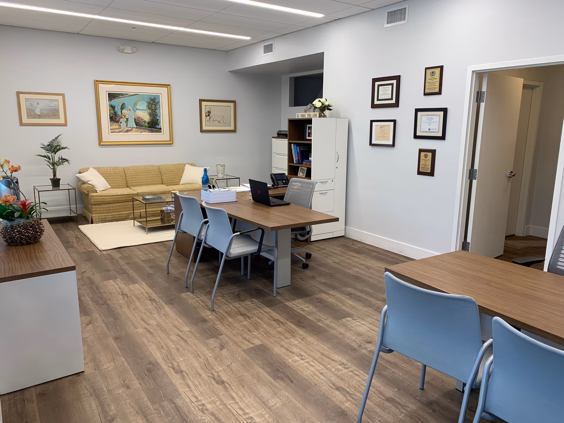 Bright reception lounge in a senior living facility with sofa, tables, chairs, plants, and framed art.