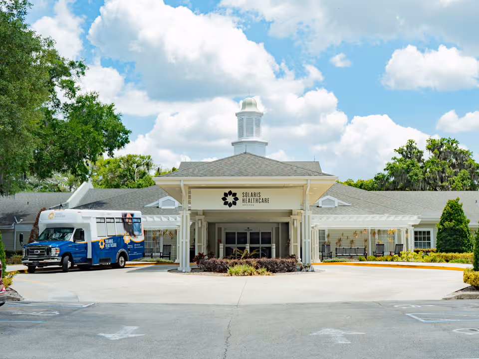 Exterior view of a healthcare center entrance with a white canopy and a blue shuttle van.