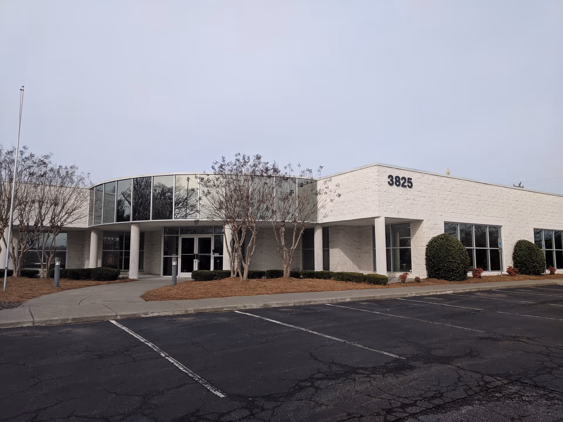 Exterior view of a white brick building with curved glass entrance and parking in front