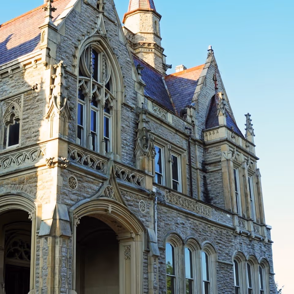 Exterior view of a historic stone building with ornate Gothic architectural details, pointed arches, and tall windows under a clear blue sky.