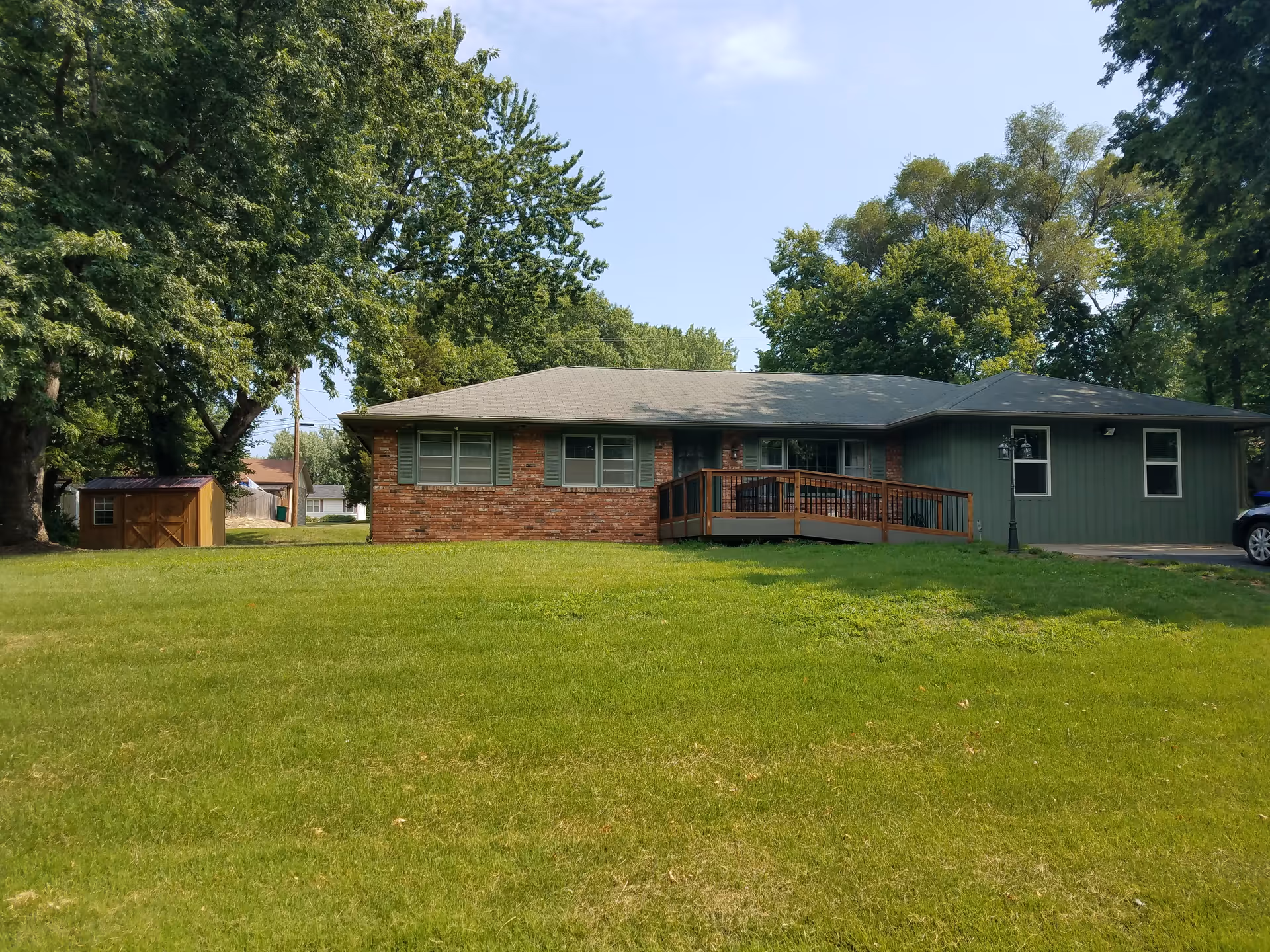 A single-story brick and green-siding senior living facility with a wooden ramp and lawn.
