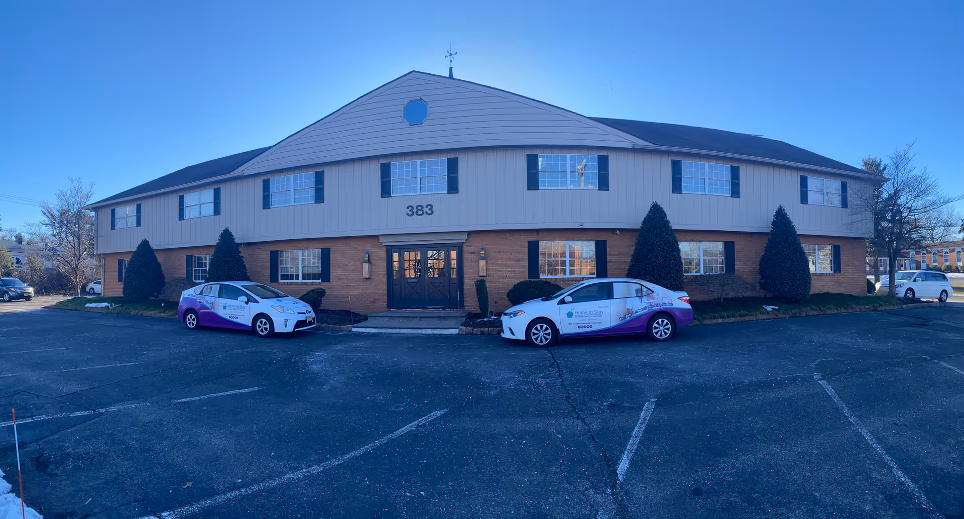 Two branded cars parked in front of a two-story brick and siding senior facility.
