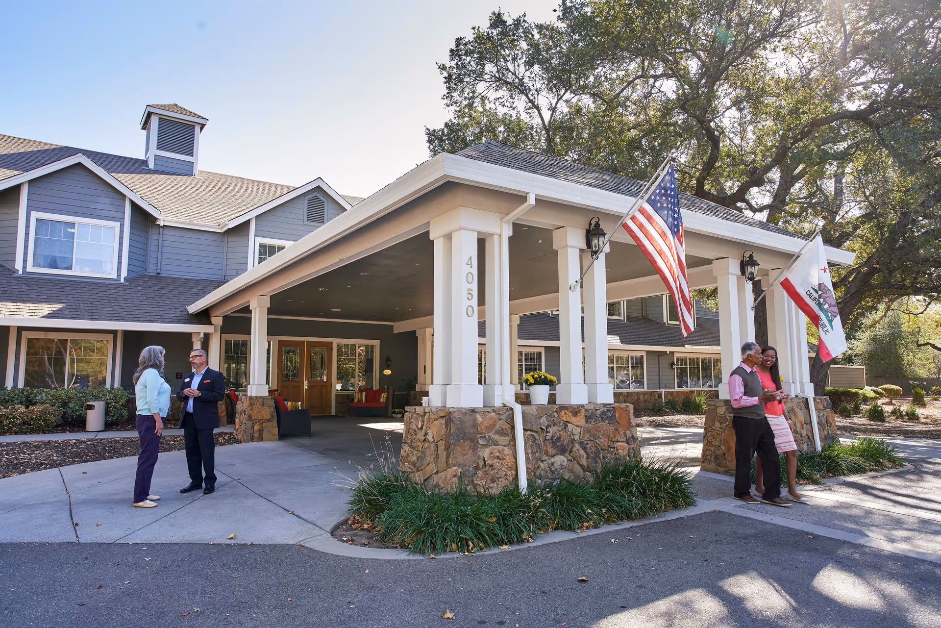 Aegis Living Carmichael entrance with flags and residents conversing outside.