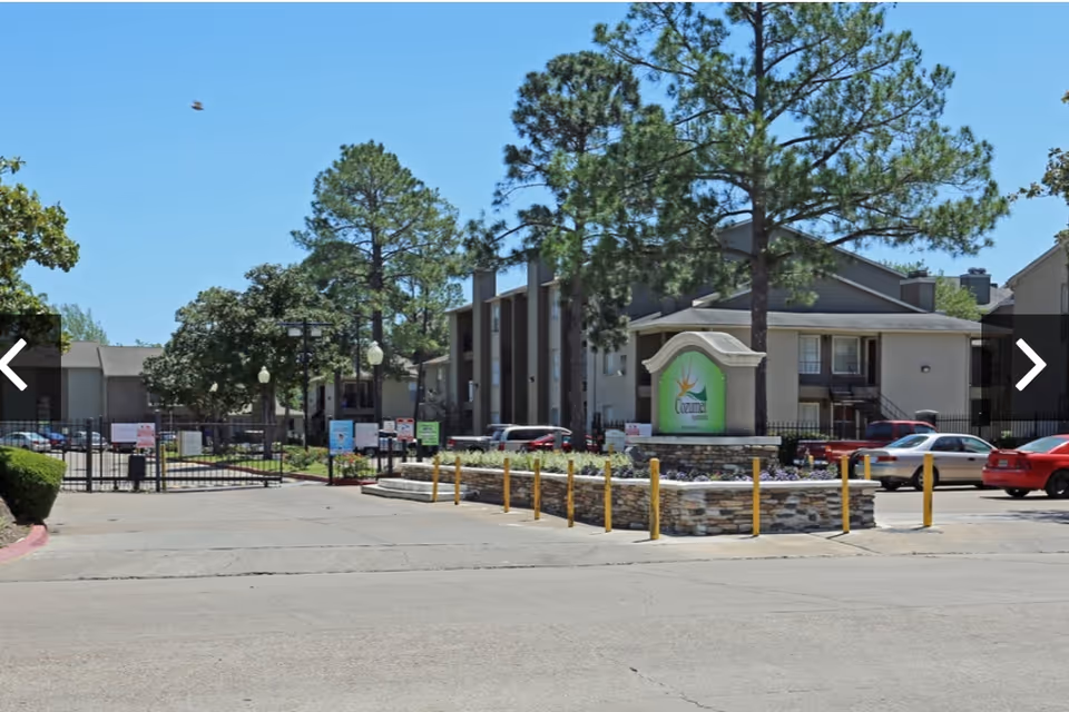 Gated entrance to a senior living building with a decorative sign and parked cars.