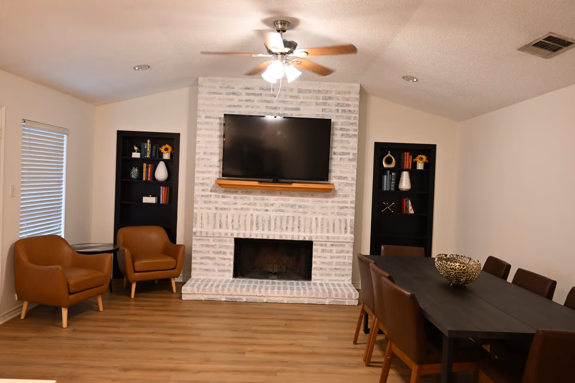 Living room with brick fireplace, mounted TV, ceiling fan, and dining table.