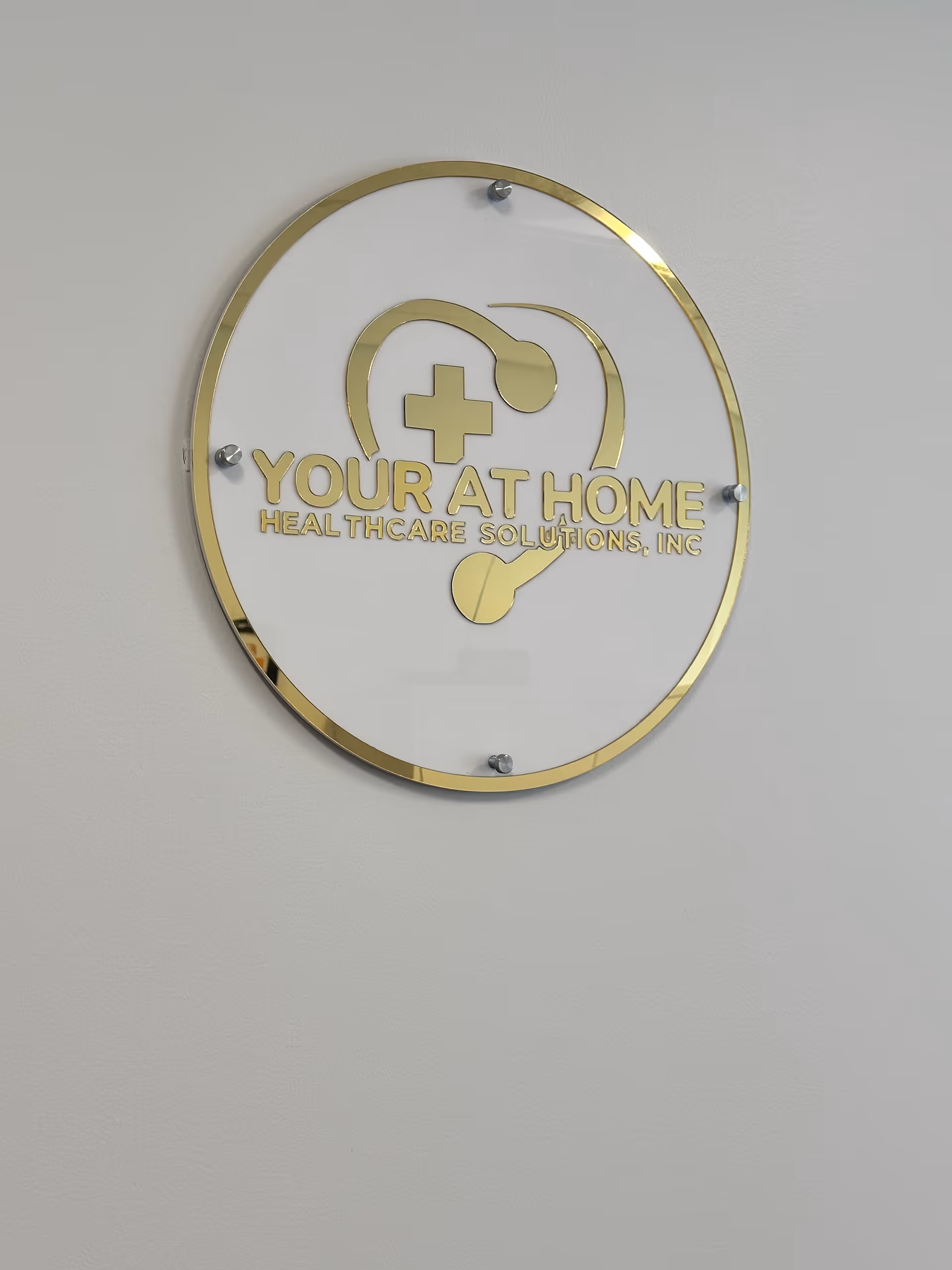 Gold-edged circular sign with stethoscope logo and text Your At Home Healthcare Solutions, Inc.