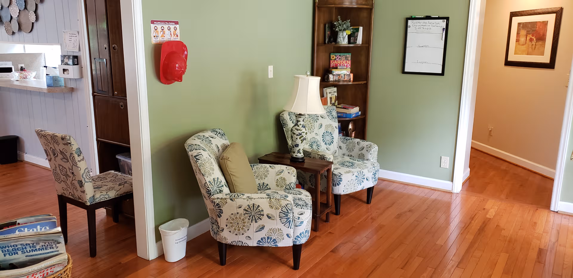 Two patterned armchairs with a side table and lamp sit in a green-walled living area.