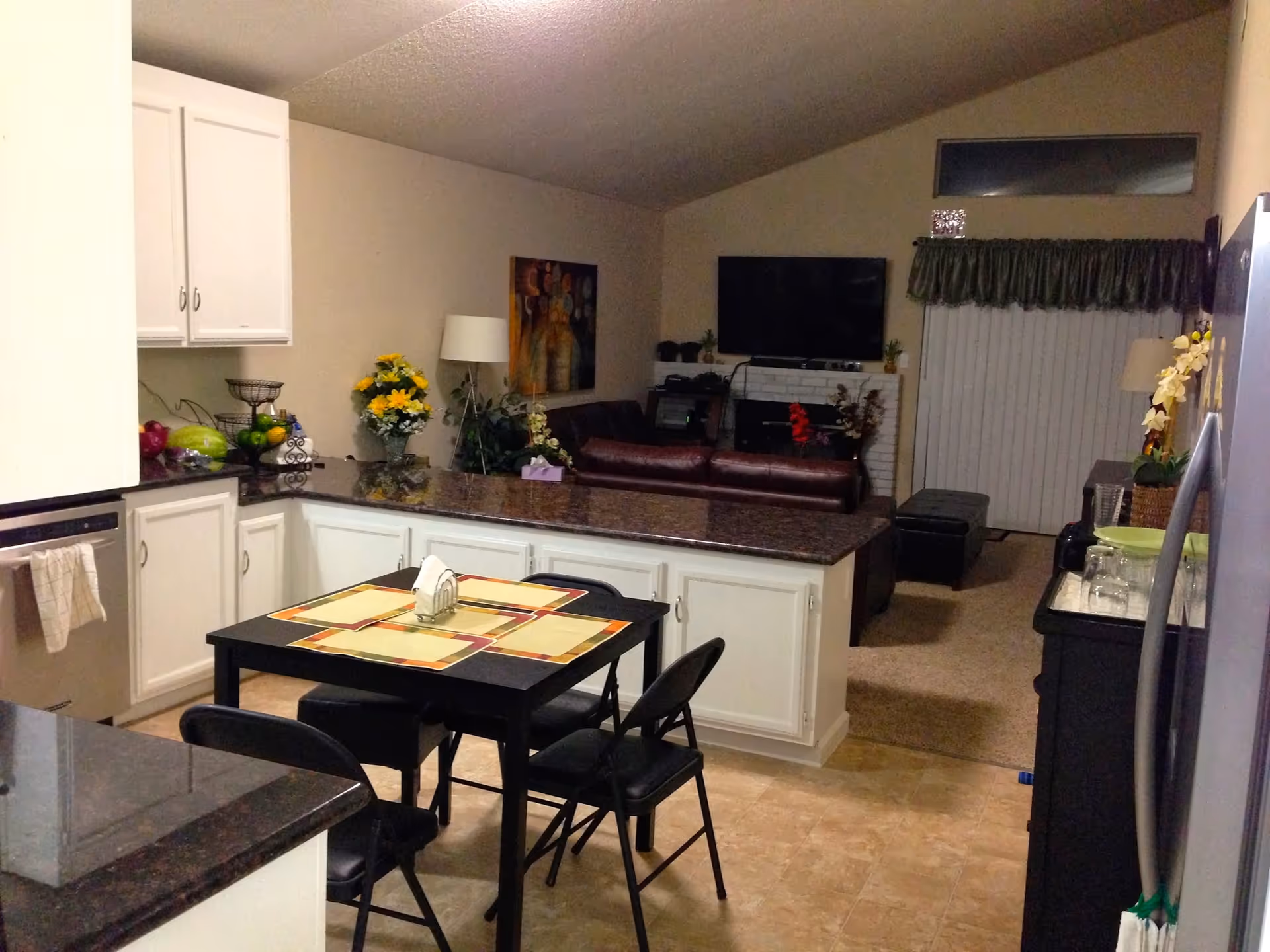 Open kitchen and living area with island, dining table, cabinets, and TV in a care unit.