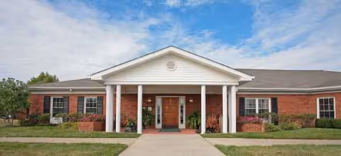 Front exterior of a single-story brick senior living facility with columns and a walkway.