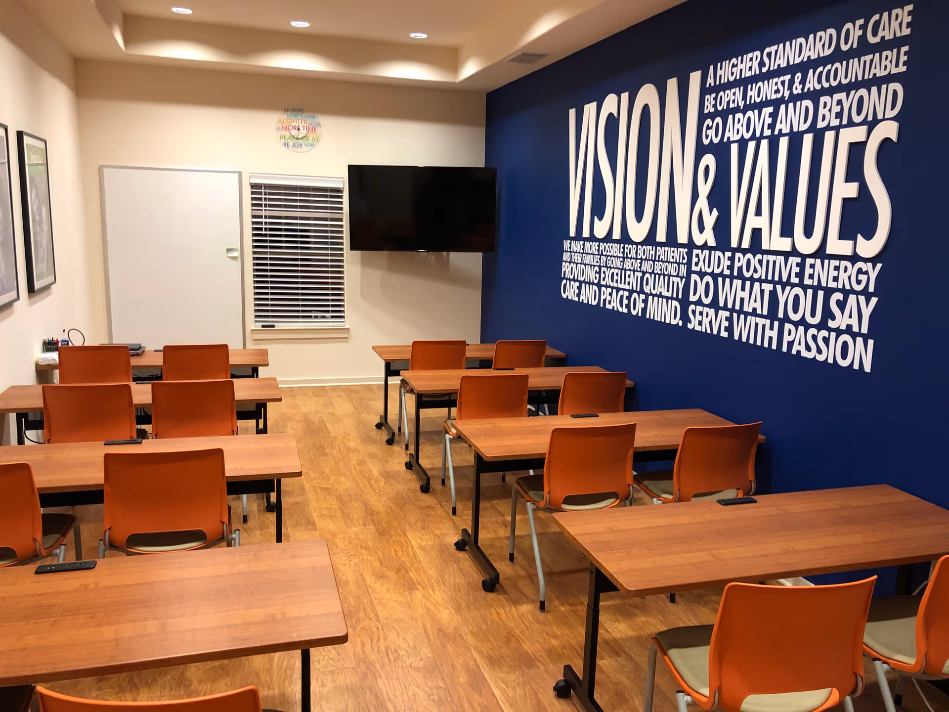 Classroom-style meeting room with orange chairs, desks, and a large Vision & Values mural.