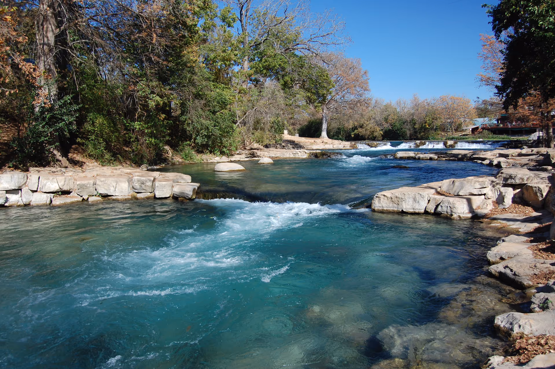 Scenic outdoor river with clear blue water, rocky banks, and trees along the shore.