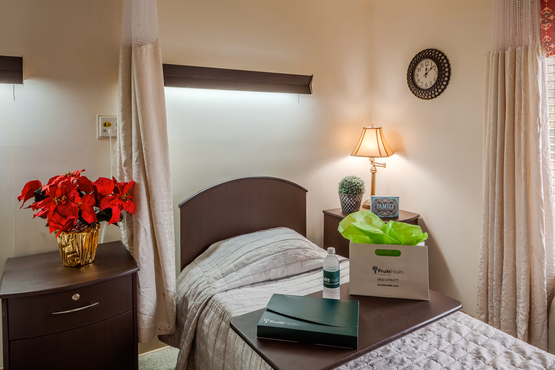 Cozy senior living bedroom featuring a bed, nightstand, lamp, plants, and curtains.