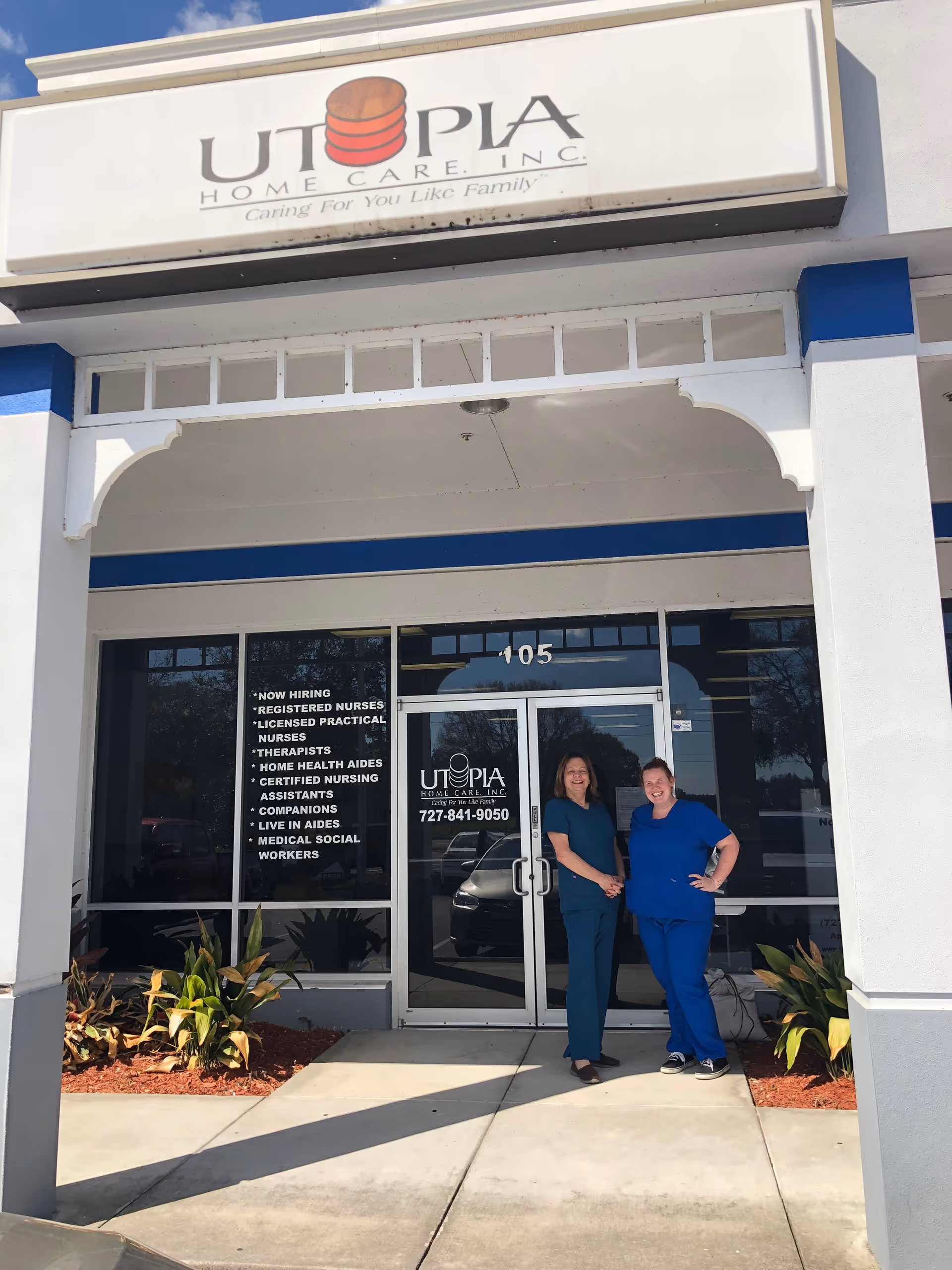 Exterior storefront of Utopia Home Care, Inc., two staff members stand at glass doors.
