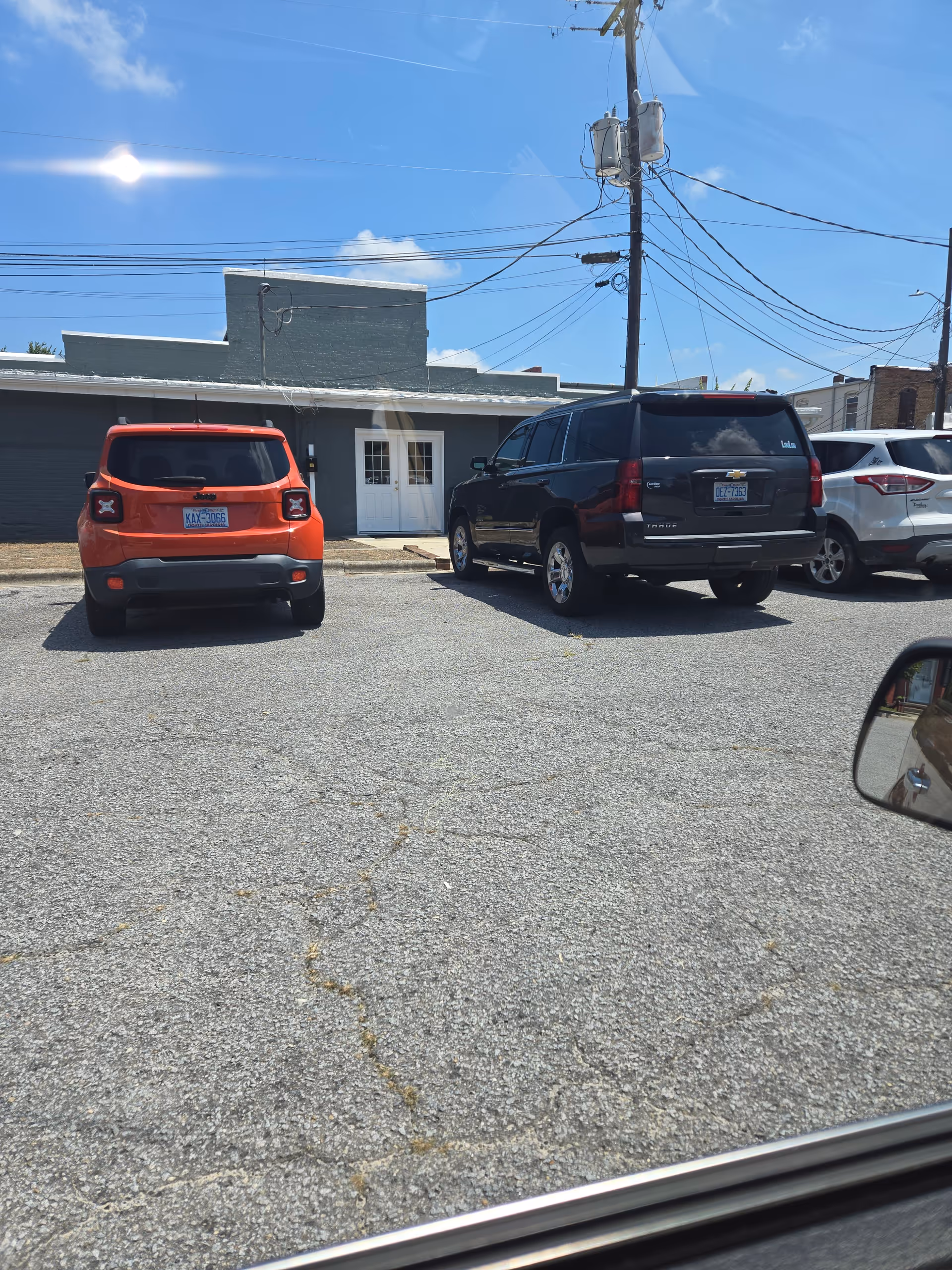 Parking lot in front of a small building with white double doors and parked cars.