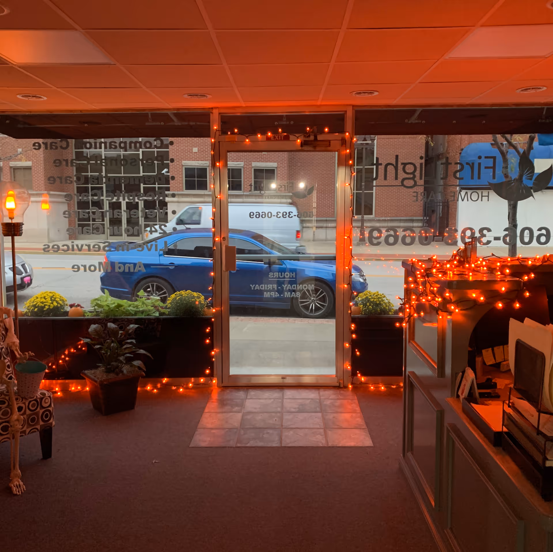 Indoor reception area with glass doors, warm orange lights, and a front desk.