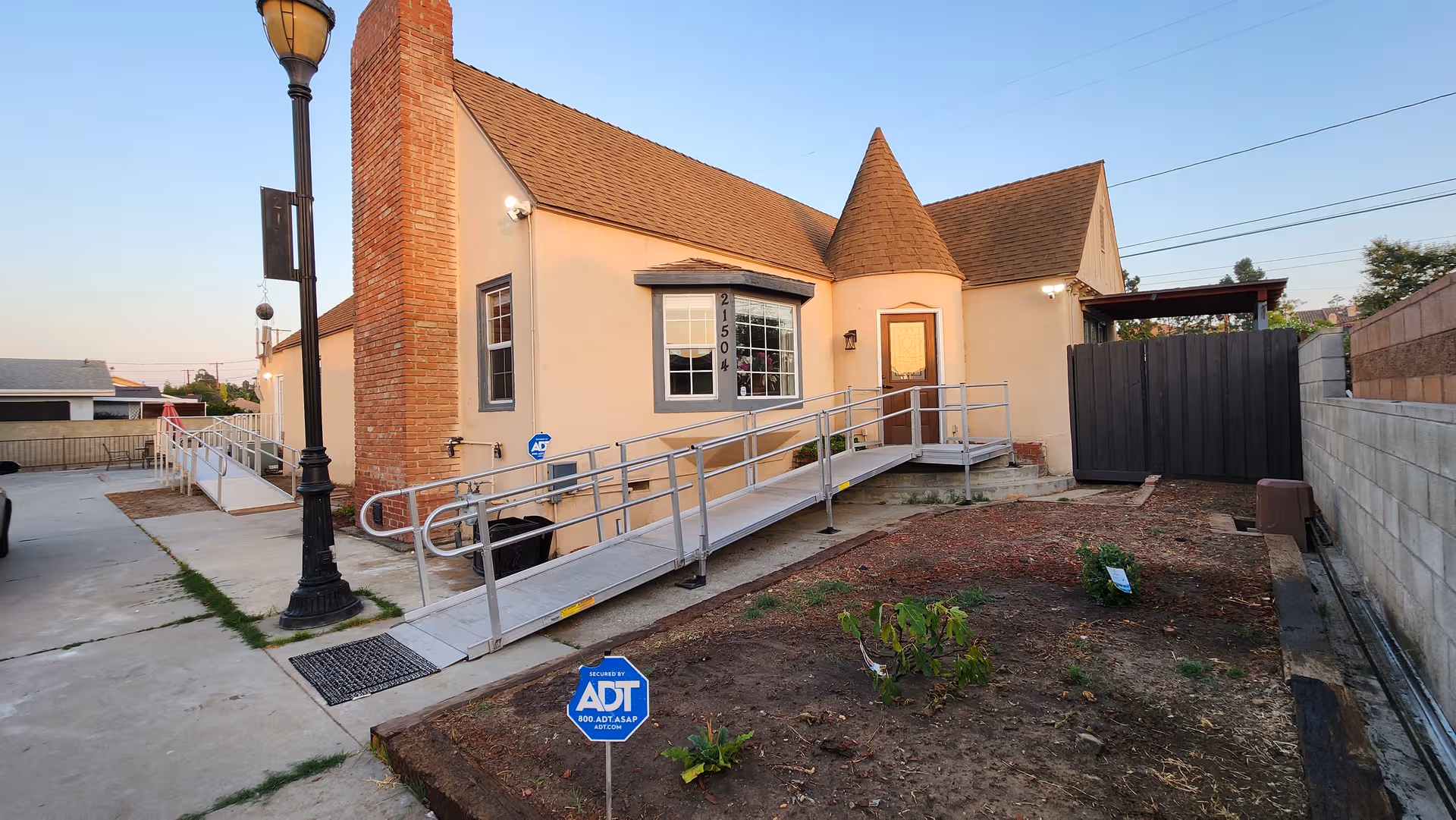 Front exterior of a beige senior care home with a wheelchair ramp and security sign.