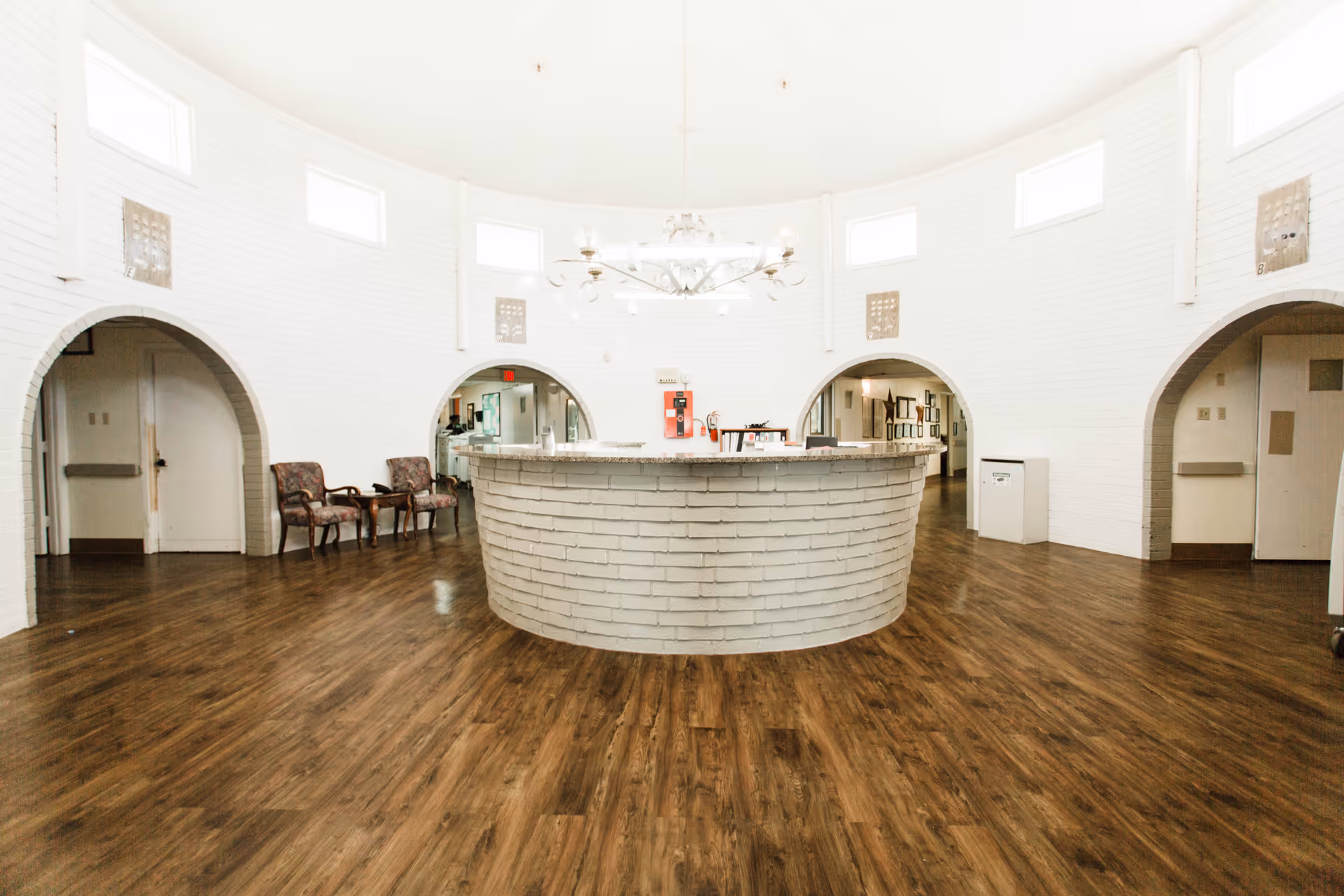 Circular front desk in a bright white lobby with arched openings and wood flooring.