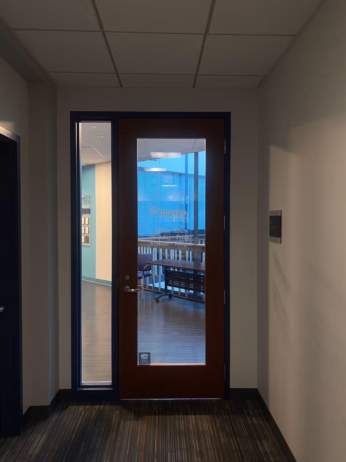 Dim hallway leading to a glass-paneled wooden door into a blue-walled room.