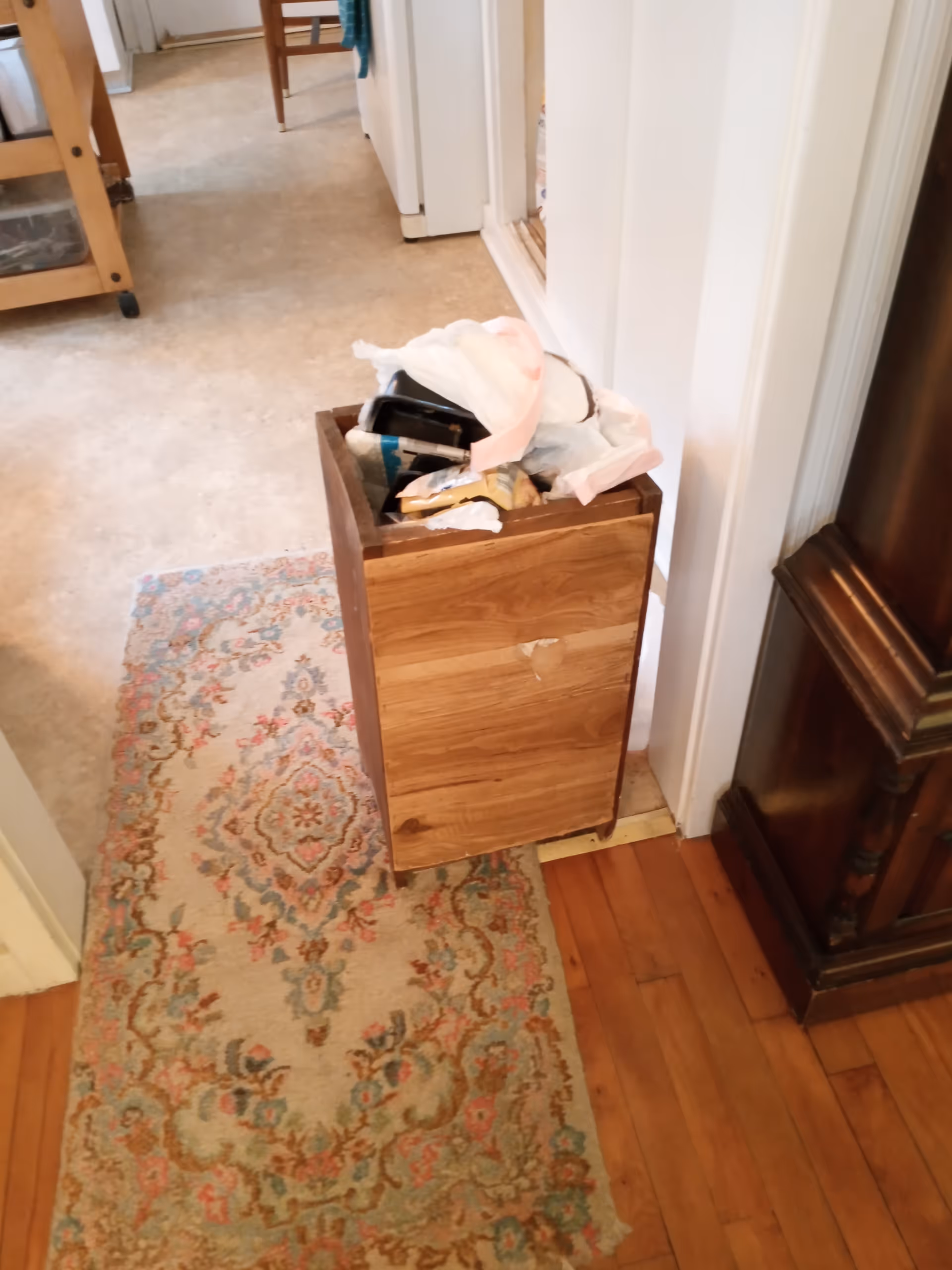 Wooden trash bin overflowing with paper and bags in a hallway of a senior living facility.