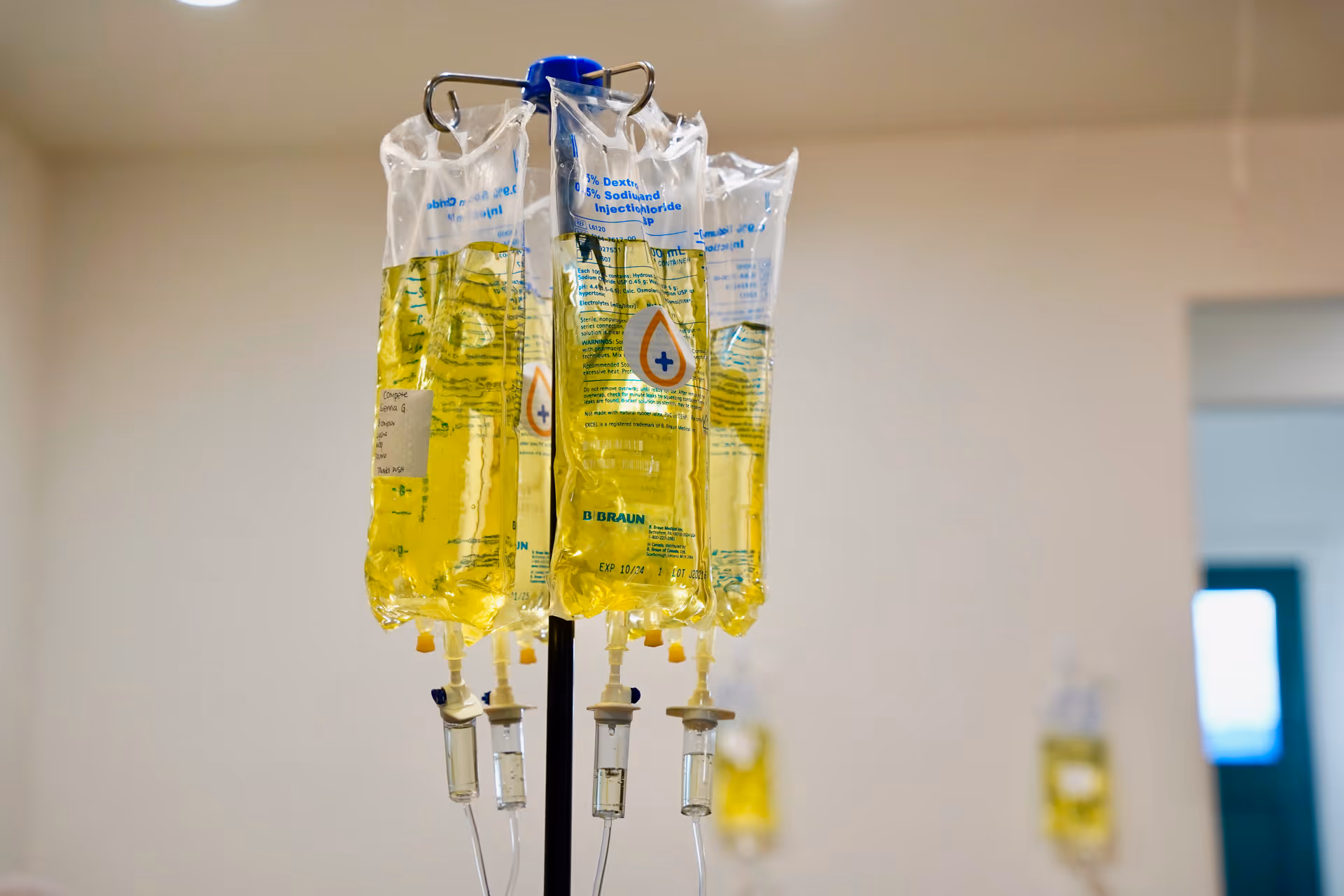 Yellow IV fluid bags hang from an infusion pole in a clinical interior.