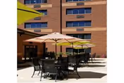 Outdoor patio with tables, chairs, and umbrellas in front of a brick building.