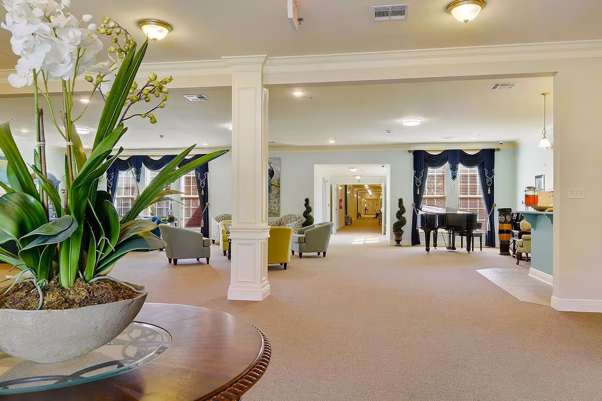 Spacious senior living common area with seating, potted plants, and a grand piano.